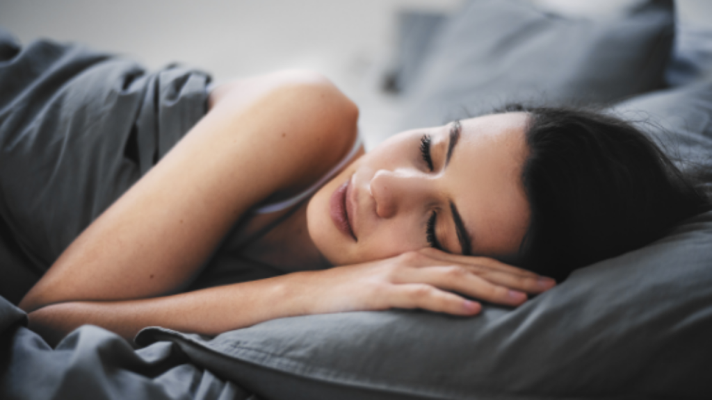 Jeune femme endormie dans un lit aux draps gris foncé
