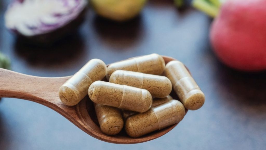 Gros plan sur une cuiller de bois remplie de capsules de supplément naturel