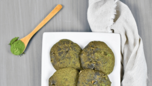 Biscuits « matcha » à la lentille d’eau verdâtre dans une assiette blanche avec une cuiller en bois contenant de la poudre de matcha