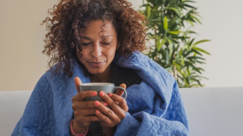 Femme avec une couverture tenant une boisson chaude pour soulager ses symptômes viraux