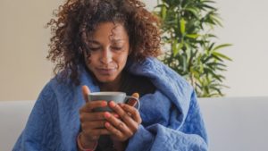 Femme avec une couverture tenant une boisson chaude pour soulager ses symptômes viraux