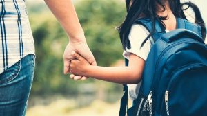 Gros plan sur un parent qui prend un enfant par la main. L'enfant porte un sac à dos.