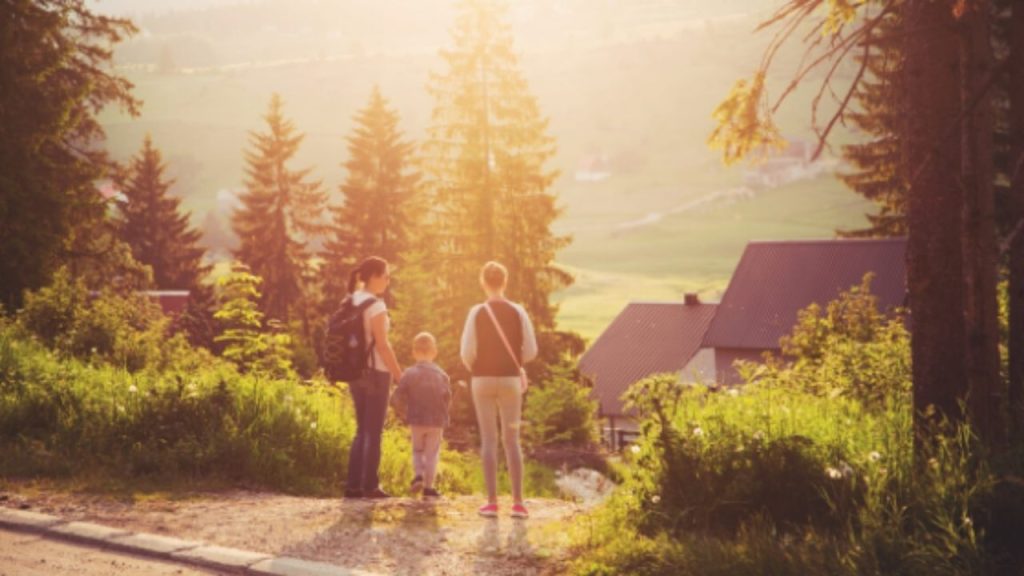 Une famille devant une maison adossée à un champ et des arbres à la campagne
