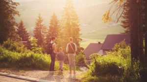 Une famille devant une maison adossée à un champ et des arbres à la campagne