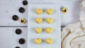 Petits chocolats blancs en forme de cœur déposés sur une assiette blanche avec en décoration des chocolats noirs