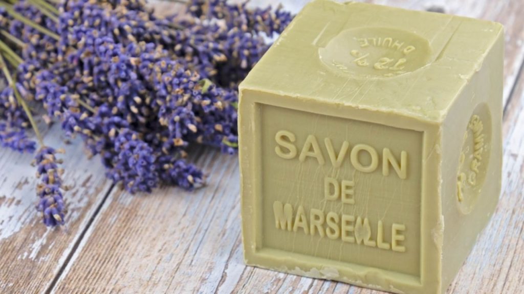 Savon de Marseille vert sur des lattes de bois et, à sa gauche, des tiges de lavande